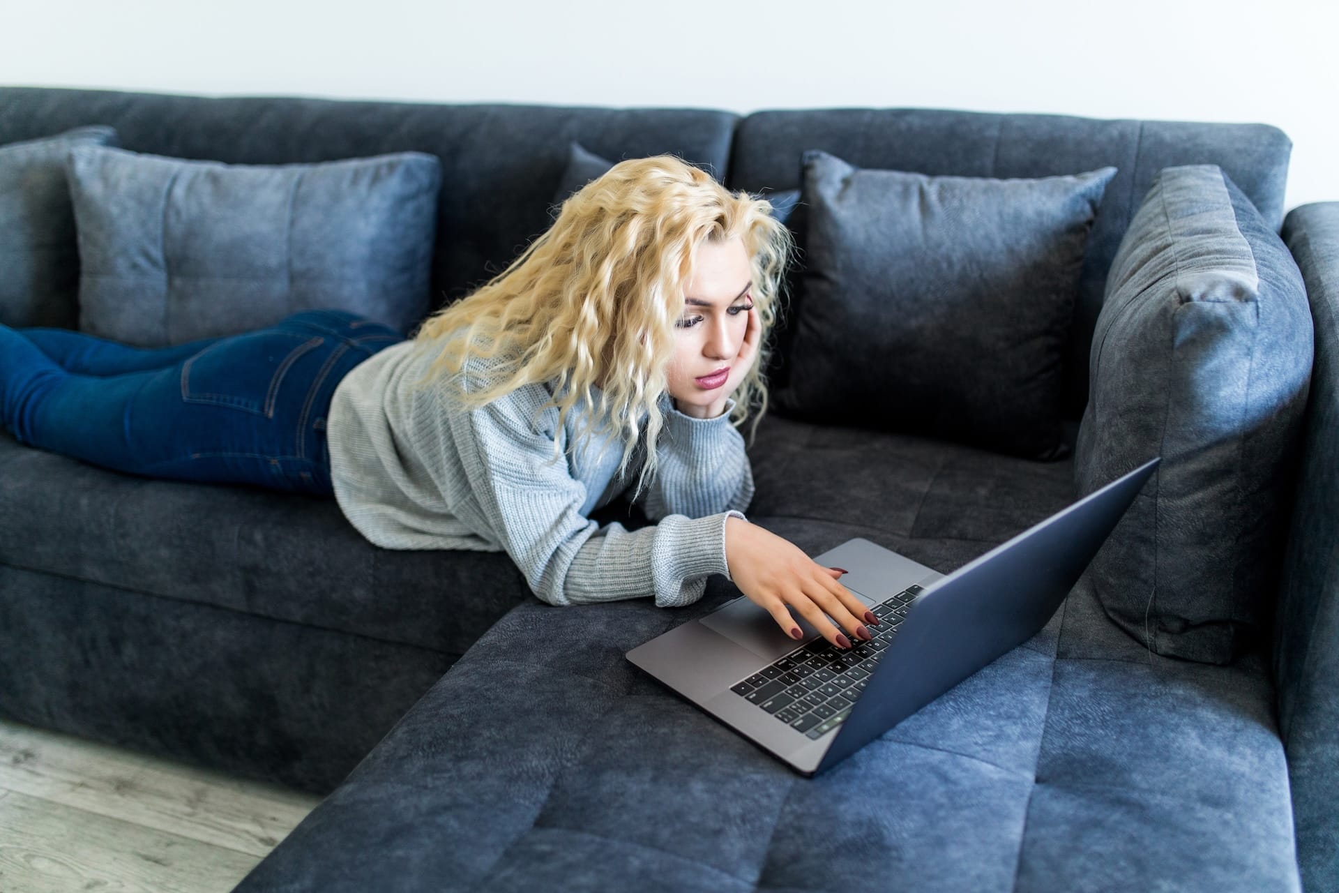 happy blonde woman working laptop sitting couch house